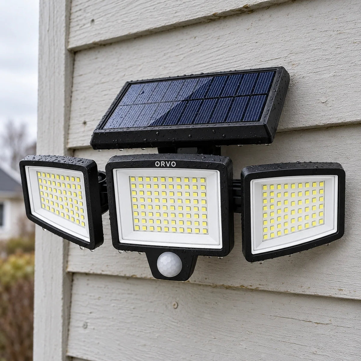 Lampada solare Orvo a tre teste accesa sopra la porta del garage al tramonto, un uomo rientra con la bici